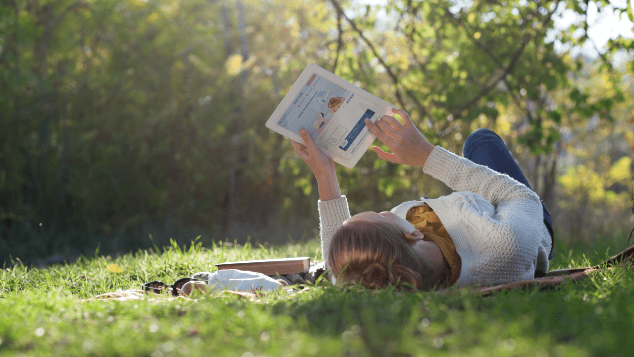 A woman lying on the grass, reading a tablet device